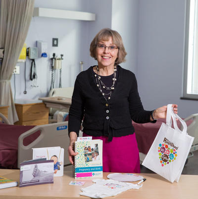 Karen Benzies, a professor in the Faculty of Nursing, along with a Welcome to Parenthood package that includes a guidebook, a onesie, and a wipe board.