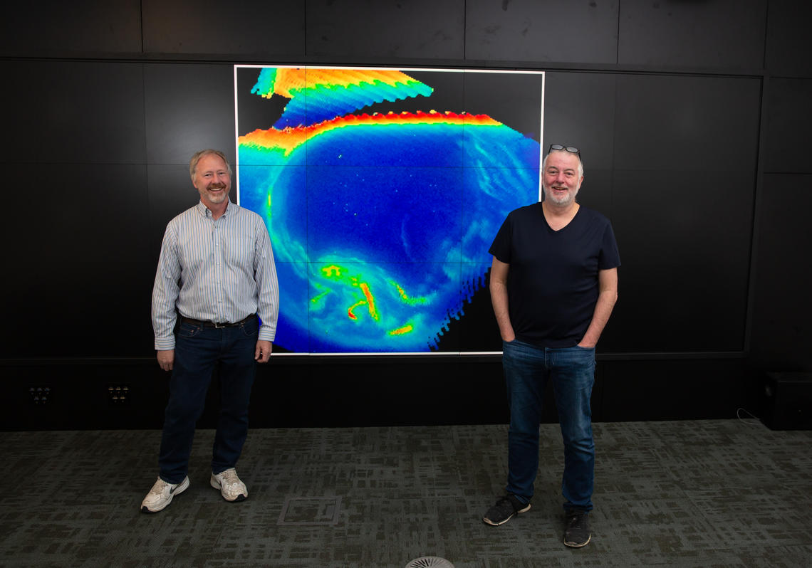 Professor Eric Donovan and SMILE-UVI Manager Greg Enno in front of an image of global auroral distribution as captured by the ISIS II satellite, which housed the first UCalgary space instrument to view the aurora.