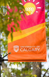 A red, yellow and orange UCalgary banner behind green trees