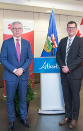 A group of three people stand in front of a podium and a set of Canadian and Albertan flags